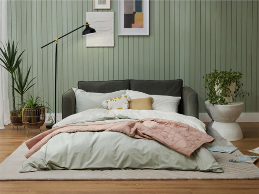Stylish bedroom with green sofa, pink and green bedding, potted plants, and wall art. Cosy and inviting space with a modern aesthetic.