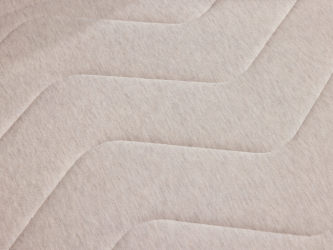 Close-up of a light grey mattress surface with a quilted, zigzag pattern. Soft texture and fabric detail visible.