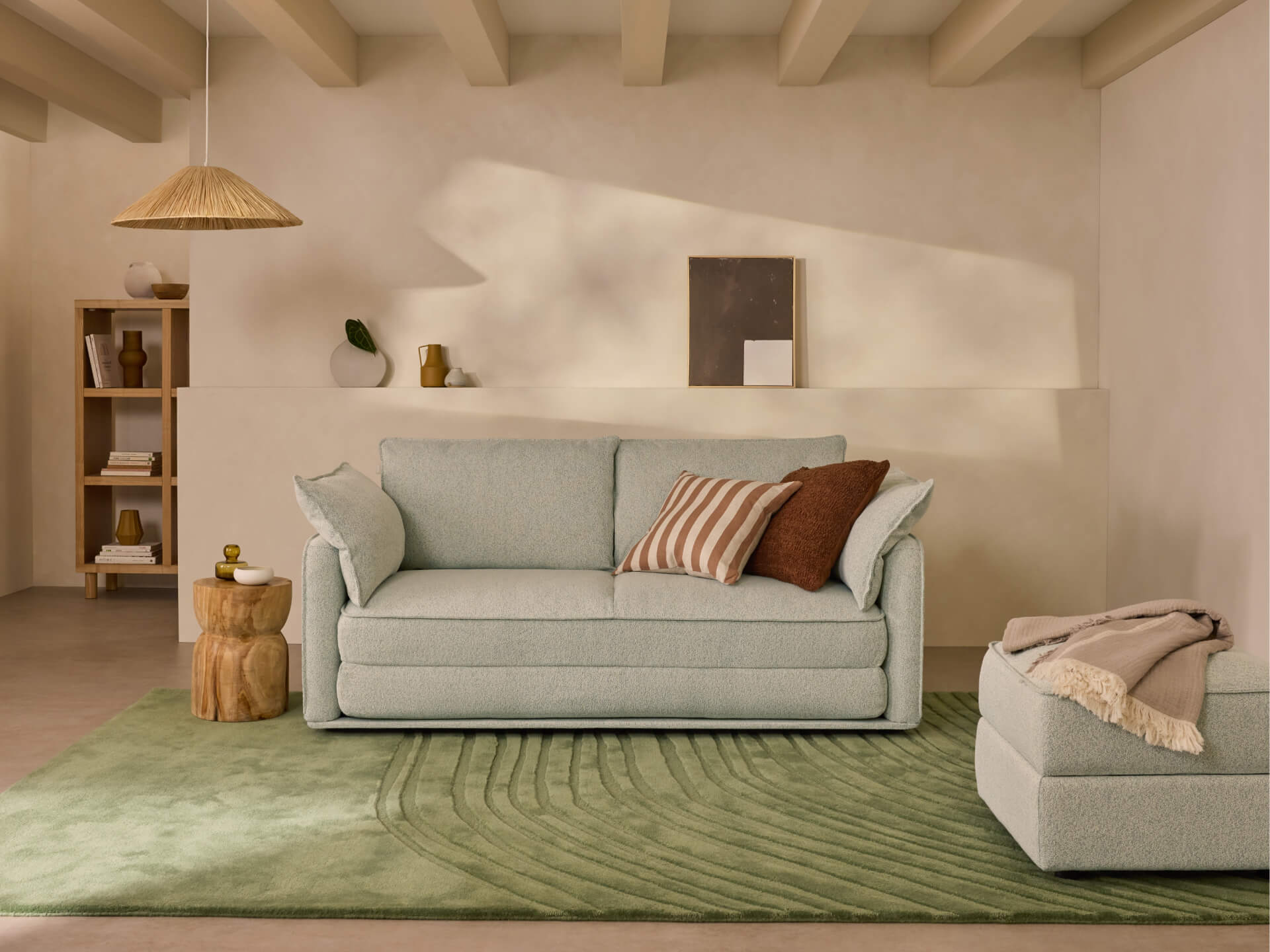 Modern living room with light grey sofa, striped cushions, and a matching ottoman on a green rug. Wooden side table and a pendant light.