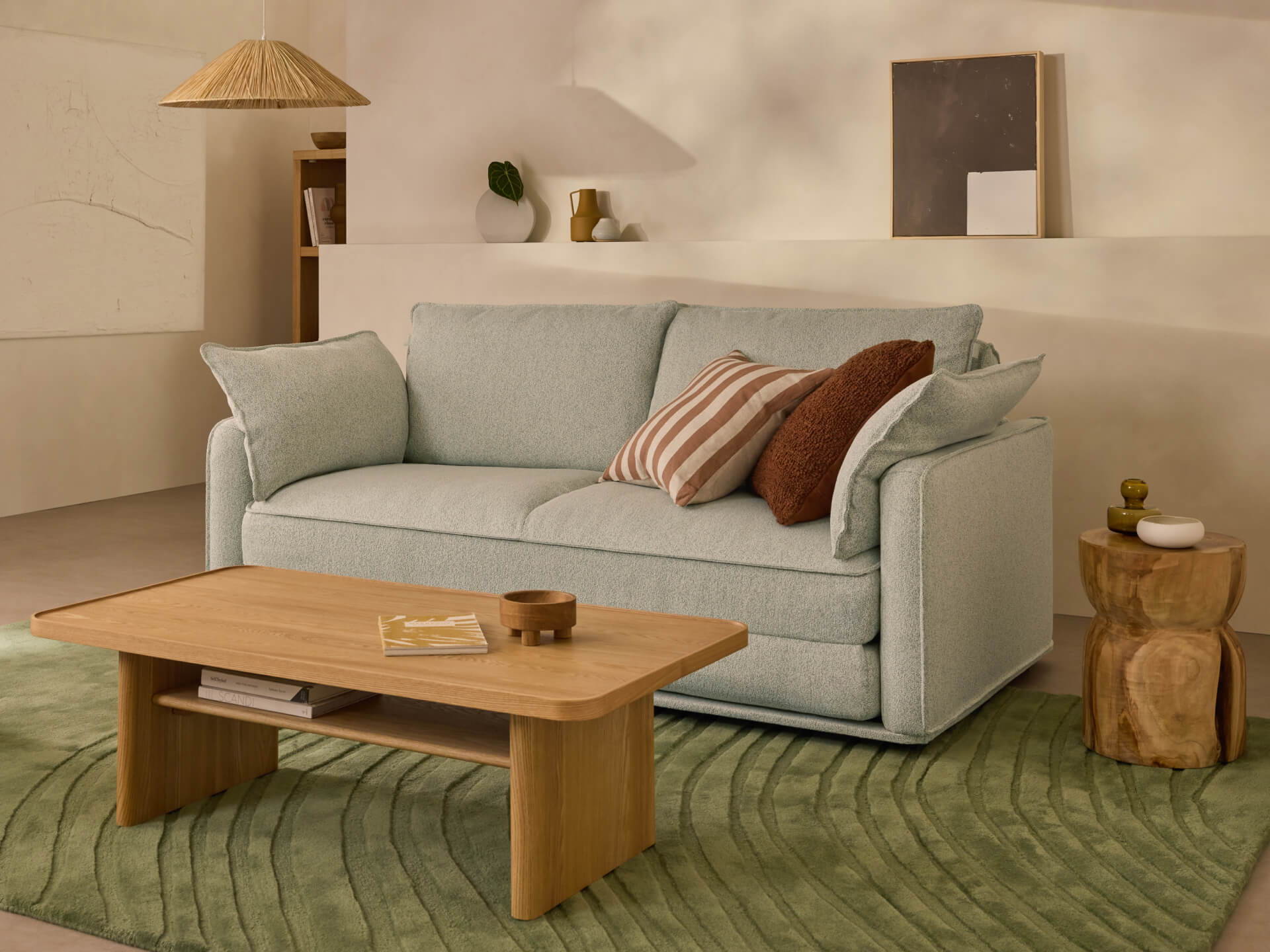 A light grey sofa with decorative cushions sits on a green rug. A wooden coffee table and rustic side table are nearby, under soft ambient lighting.