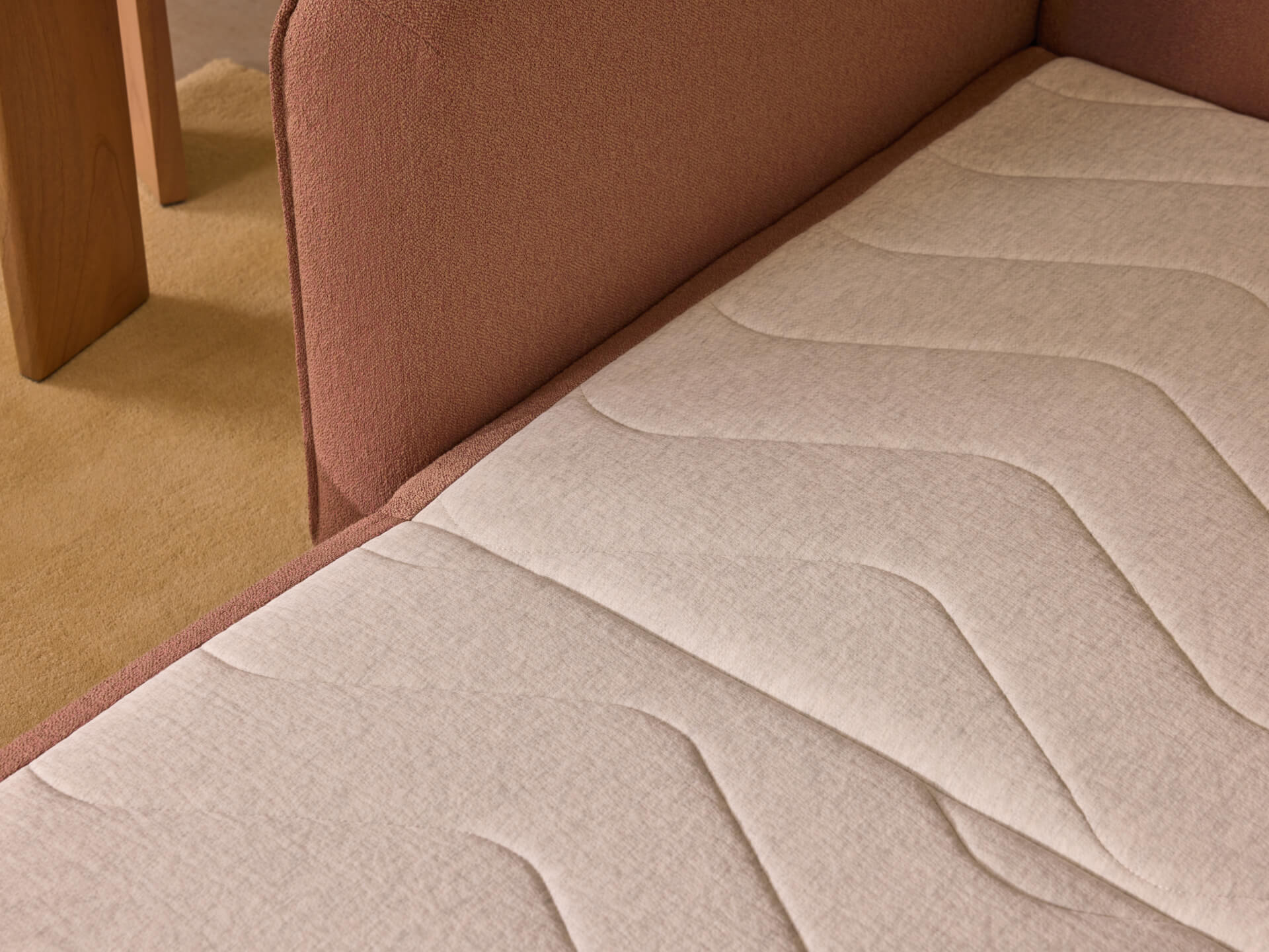 Light brown couch with panelled beige cushion detailing, set against a soft beige carpet and adjacent wooden table.