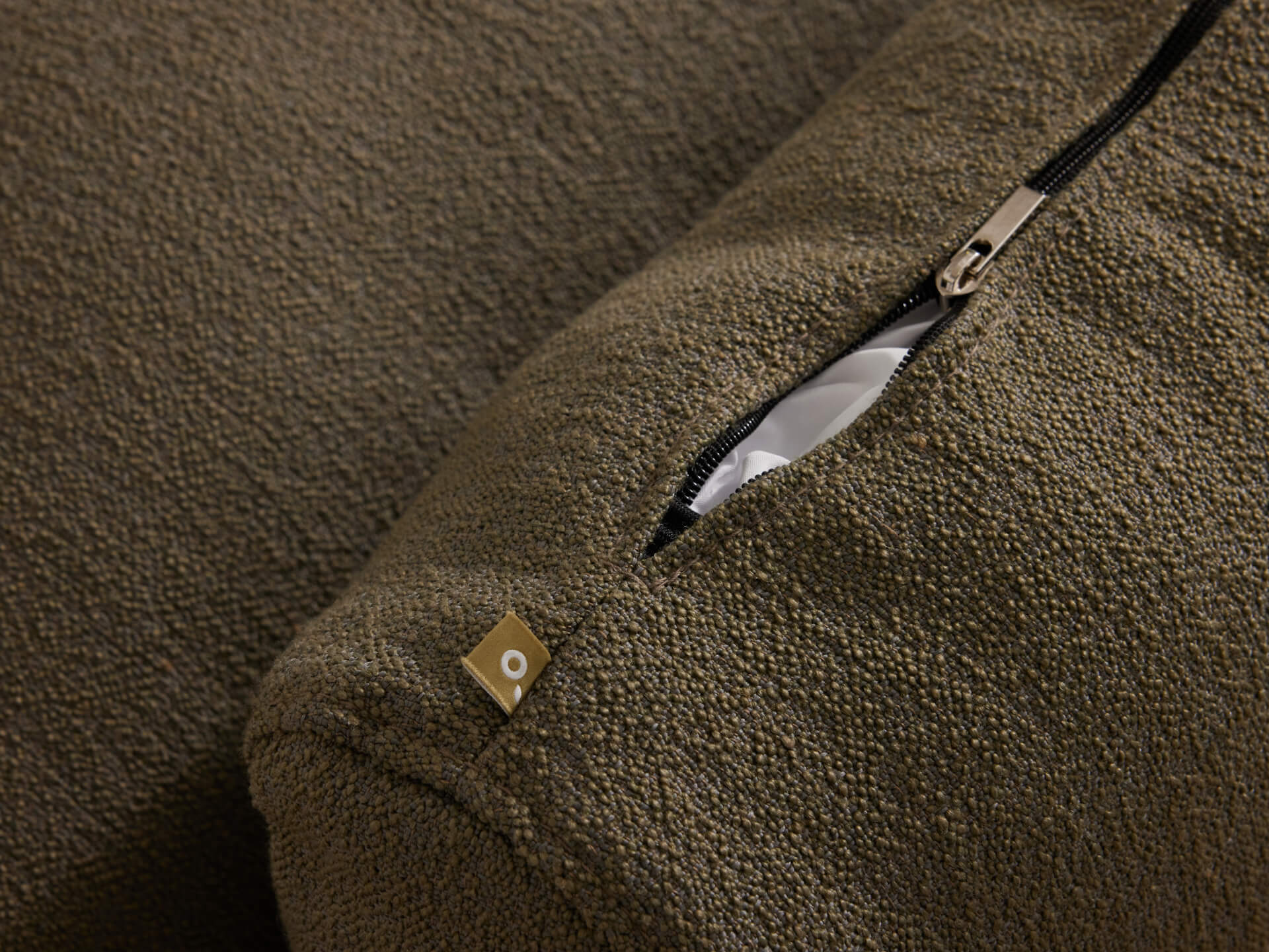 Close-up of olive green textured cushion cover with visible zippered opening and small metallic tag detail.