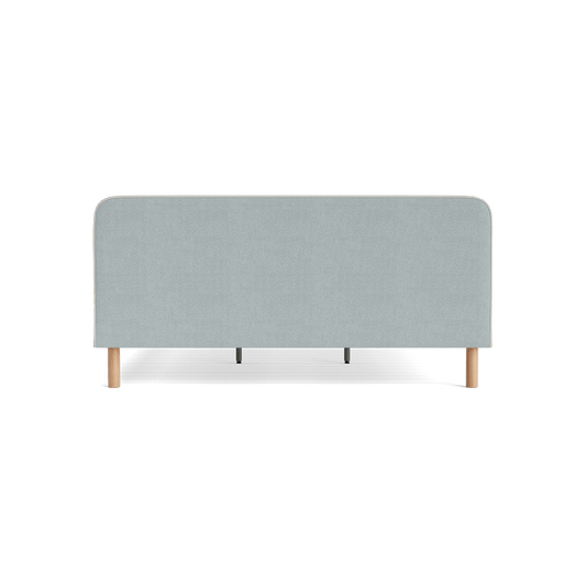 Light grey fabric bed headboard with rounded top edges, supported by light wood legs. Minimalist and modern bedroom furniture design.