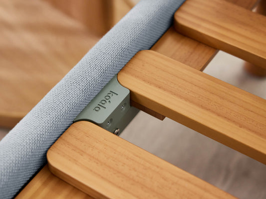 Close-up of a wooden bed frame with light grey fabric detailing and a visible metal bracket.