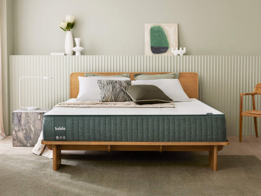 A modern bedroom with a wooden bed frame, green mattress, white and green pillows, and neutral decor.