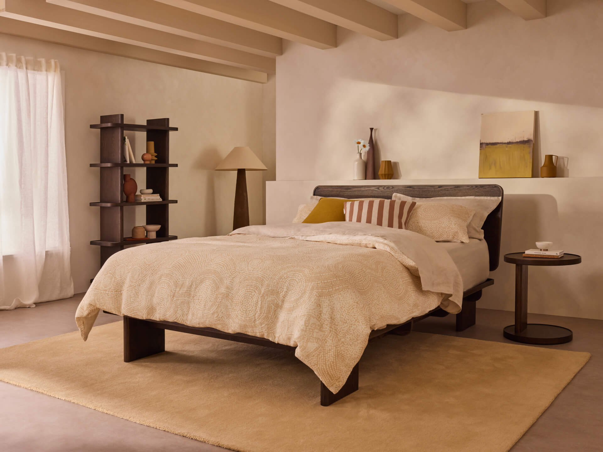 Modern bedroom with a wooden bed, cream bedding, dark bedside table, tall bookshelf, and a large window. Neutral tones and minimalist decor.