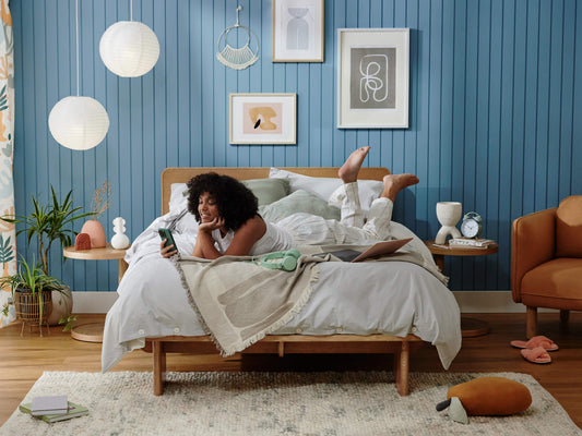 Cosy bedroom with blue panelled wall, wooden bed, white bedding, and wall art. Soft lighting and plants complete the warm, inviting decor.
