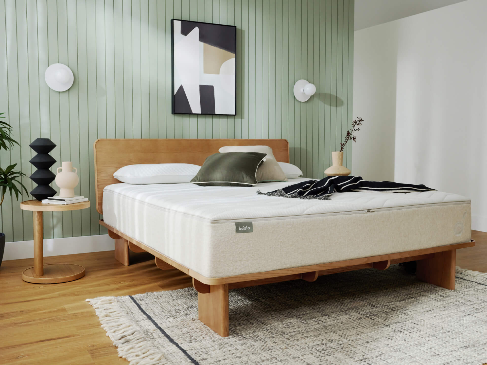 Modern bedroom with a light brown bed, beige mattress, green pillow, side table, and abstract art on a mint green panelled wall.
