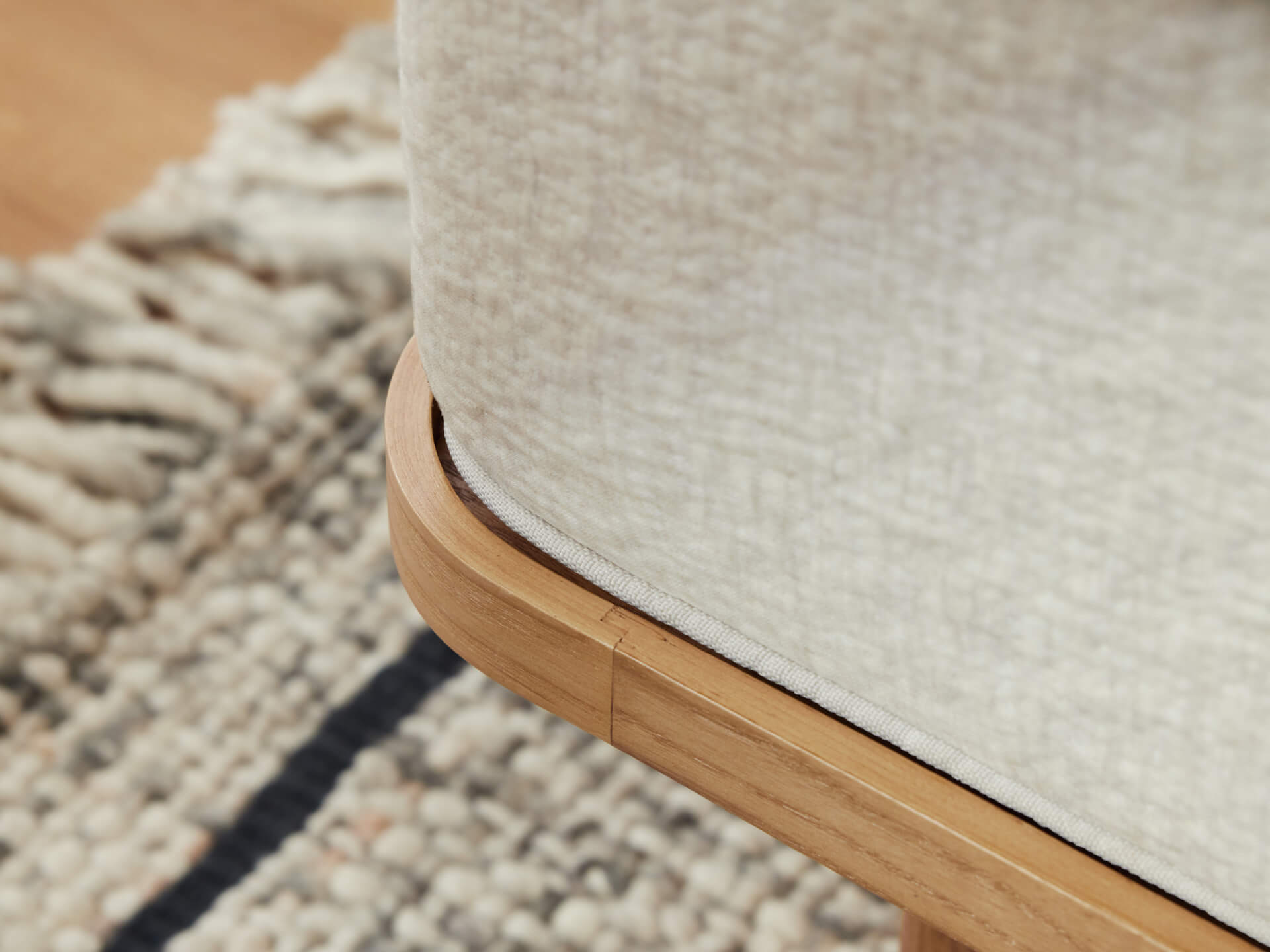 Close-up of a light beige upholstered sofa corner with a rounded wooden base, set on a textured cream and black patterned rug.