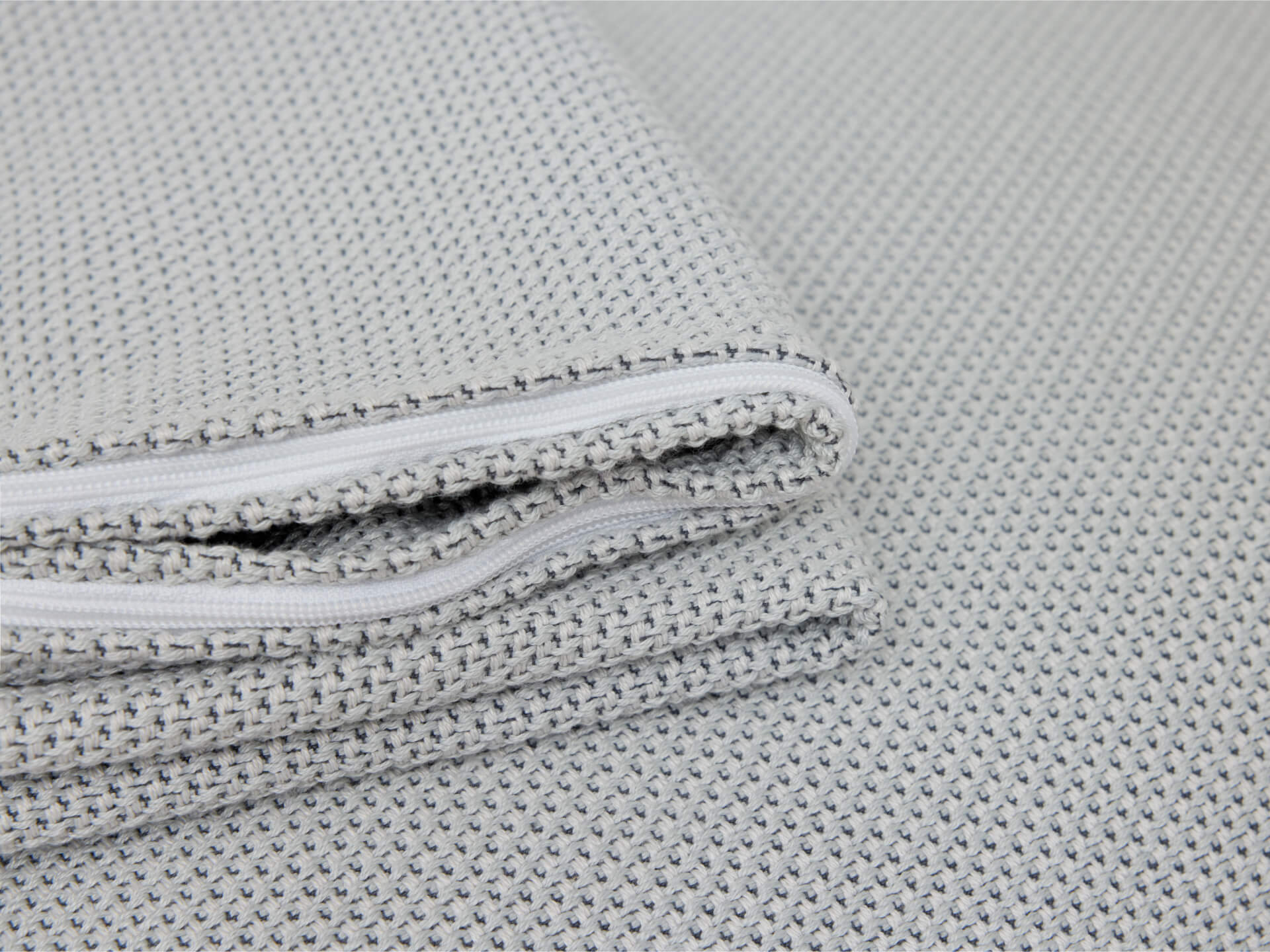 Close-up of folded light grey textured fabric with a visible white zip.