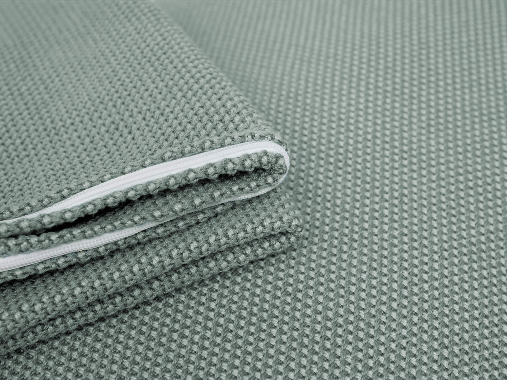 Close-up of folded, textured light green fabric with a visible white zipper, suitable for upholstery or furniture coverings.