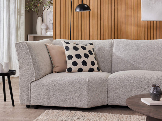 Light grey sectional sofa with beige and black polka dot cushions in a cosy living room. Features wood panel wall and round coffee tables.