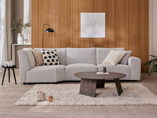 Modern living room with a light grey sofa, patterned cushions, dark wood coffee table, and wood-panel feature wall. Natural tones and textures.