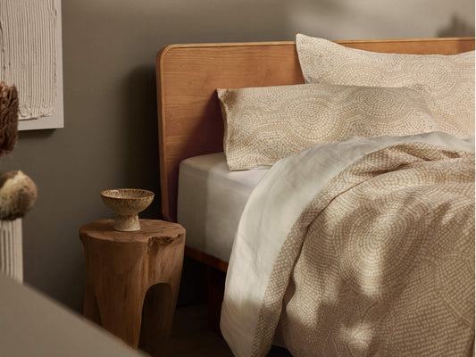 Stylish bedroom with a wooden bed, beige patterned bedding, and a rustic wooden side table holding a decorative bowl.