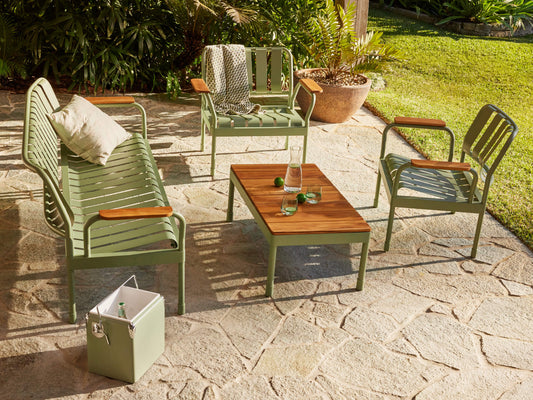 Outdoor furniture set with light green metal and wooden accents. Includes a lounge, two chairs, and a table on stone paving. Cooler nearby.