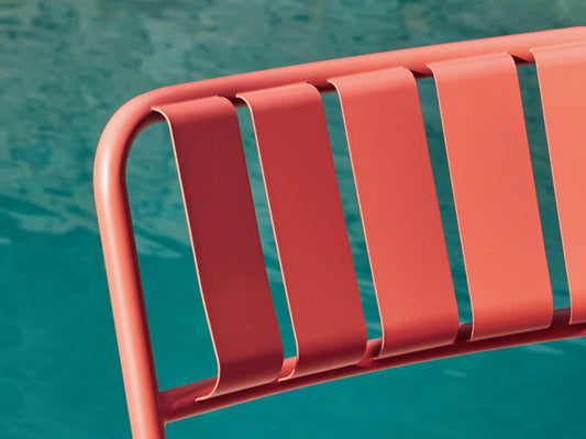 Close-up of a red metal chair with slatted backrest, positioned against a teal background.