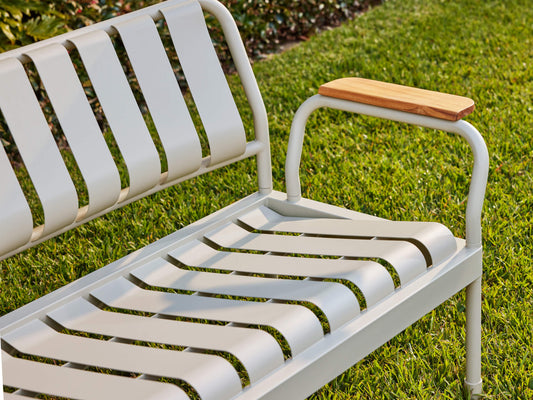 Outdoor metal bench with grey slats and a wooden armrest on green grass. Perfect for garden seating or patio furniture.