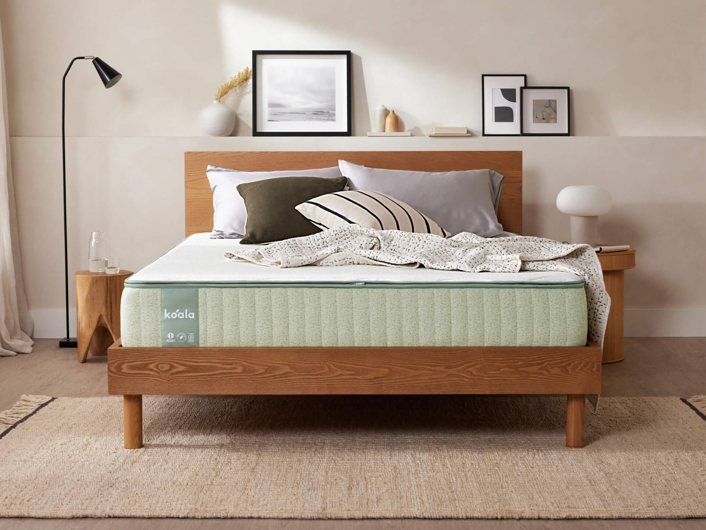 Modern bedroom with a light green mattress on a wooden bed frame, white and grey bedding, art on wall, and minimalist decor on a beige rug.