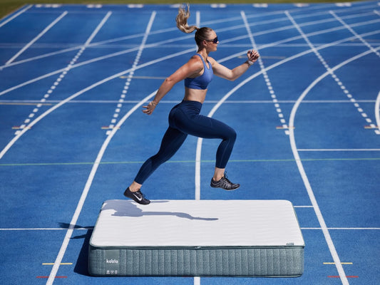 Athlete in workout gear runs on a white and grey mattress placed on a blue athletics track.