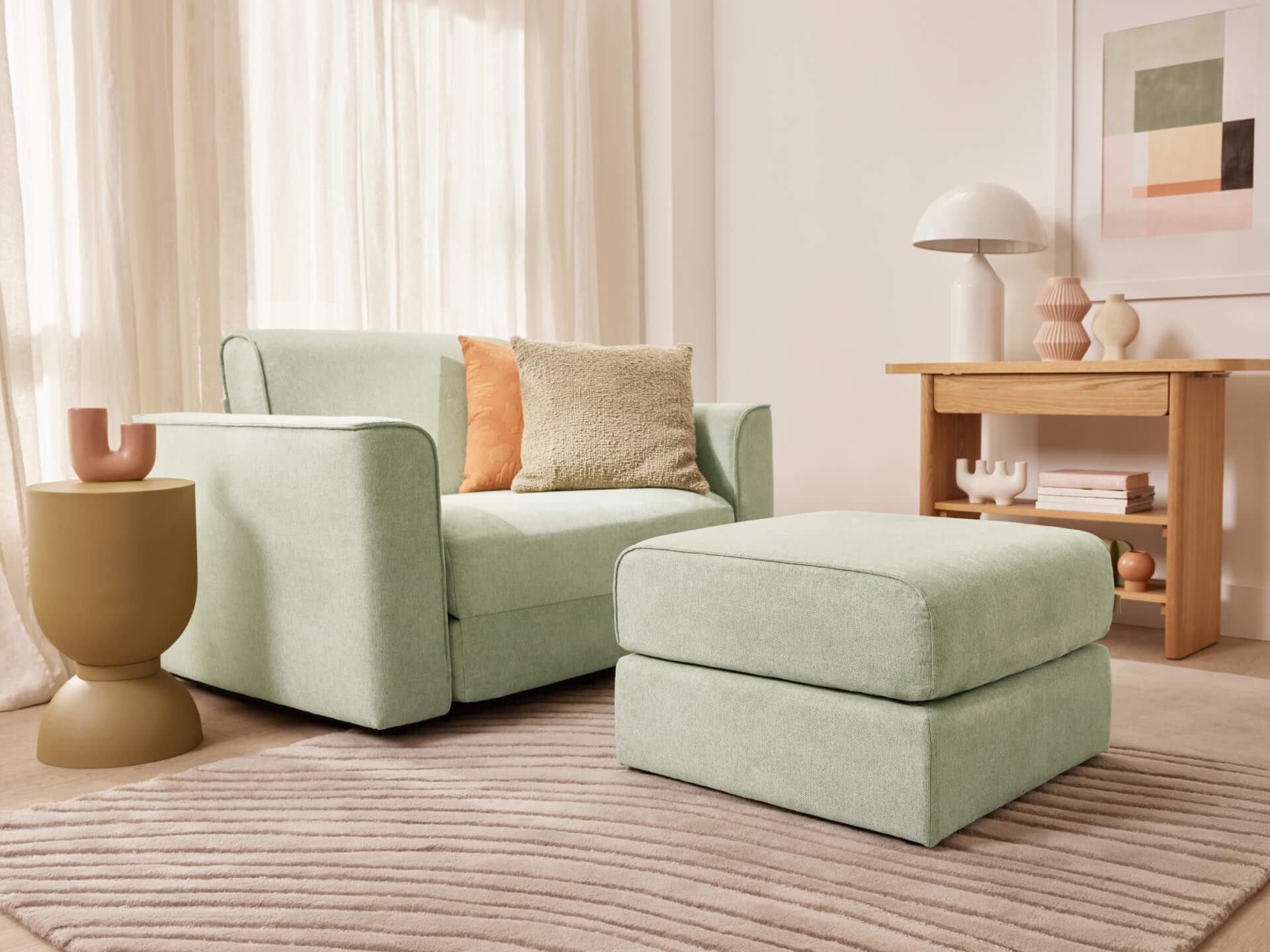 A light green armchair with an ottoman, beige and orange cushions, a brown side table, and a wooden console in a cosy living room with a striped rug.