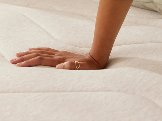 Hand pressing into a light beige mattress, showcasing its softness and comfort.