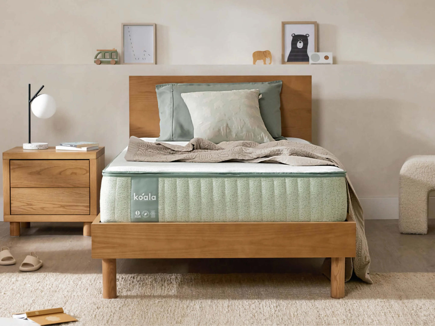 Bedroom with a wooden bed frame, green mattress, and matching bedside table. Decor includes framed art, a small lamp, and a rug.