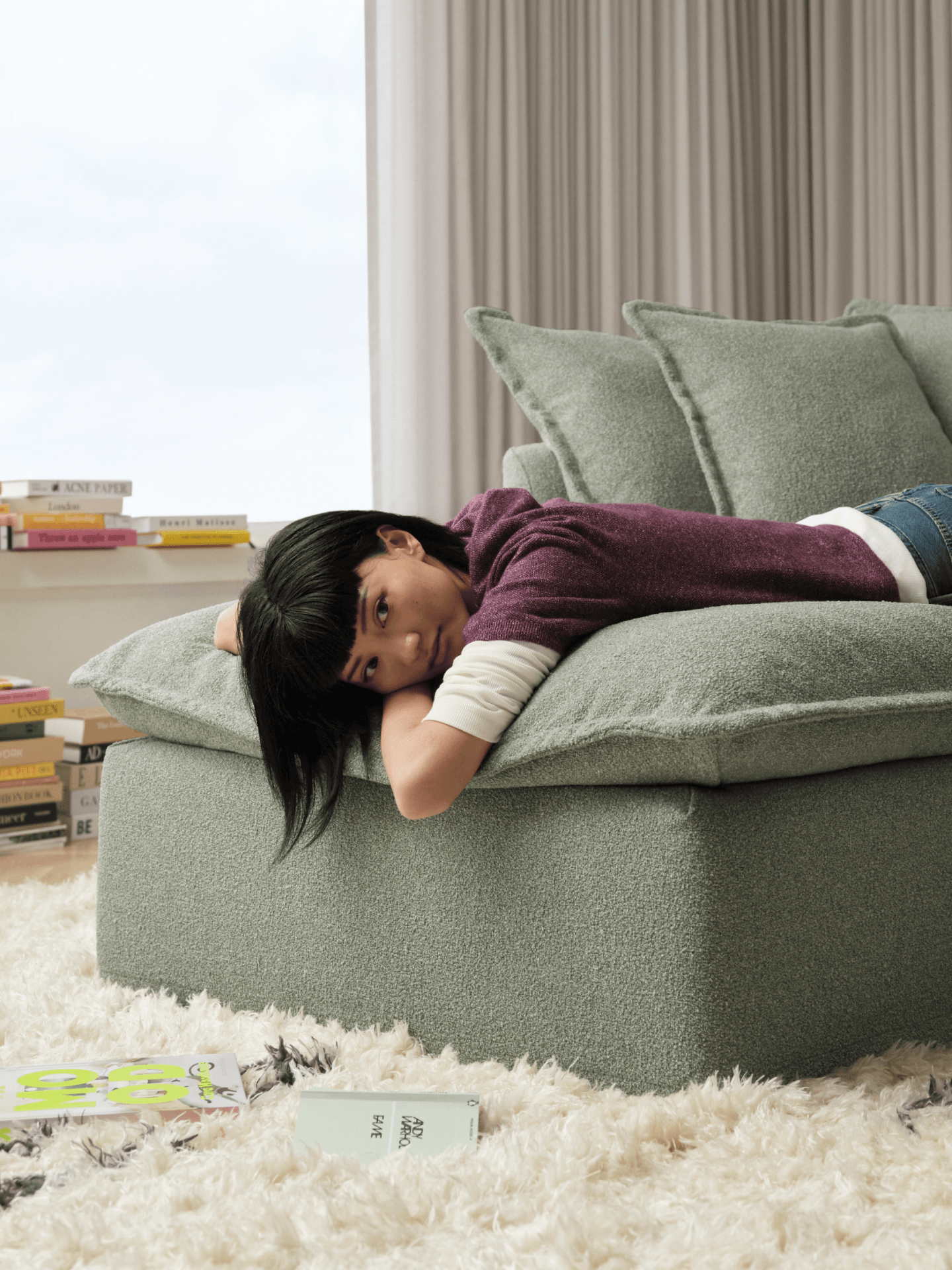 Child relaxing on sage green boucle Koala sofa with books and shag rug in living room