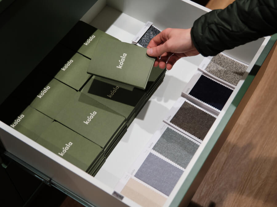 A person selects an olive green fabric sample from a drawer filled with various fabric swatches and samples.