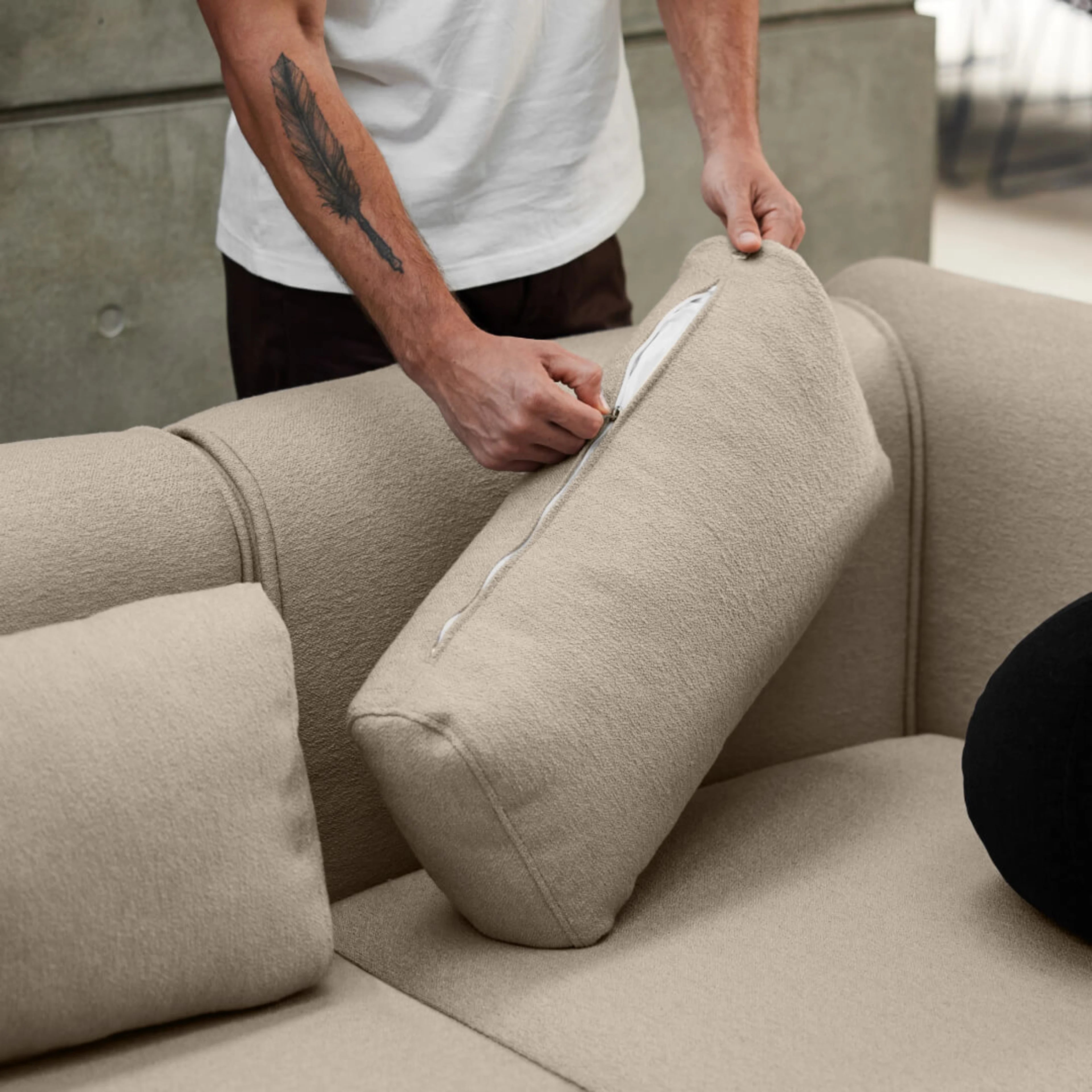 Person adjusting beige sofa cushions with zippers, showing soft fabric texture in a modern living room setting.