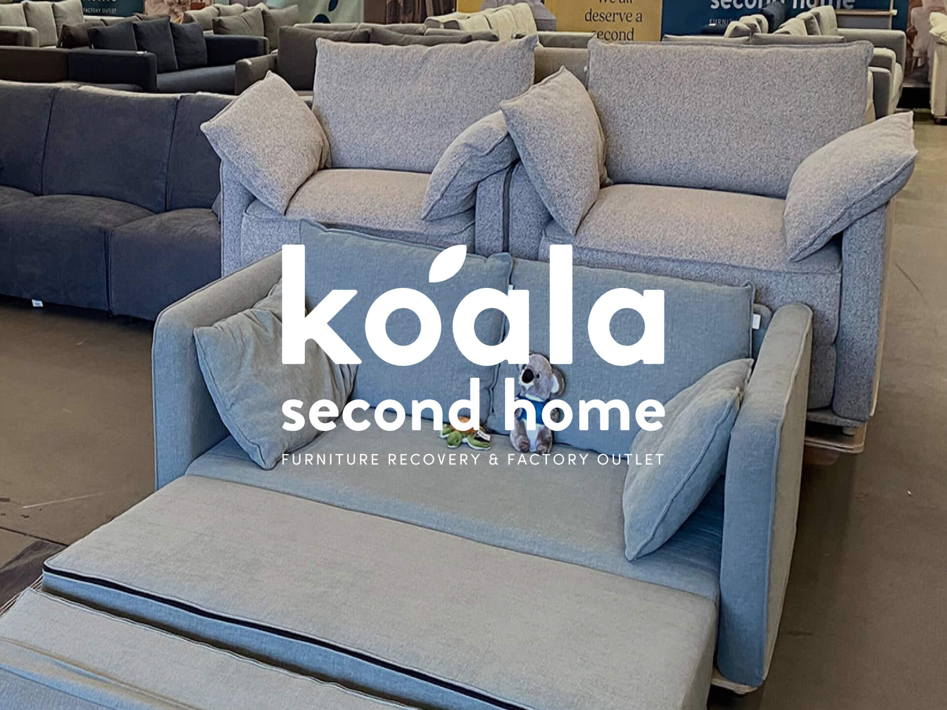 Showroom of sofas and armchairs in light grey and blue, with "Koala Second Home" text overlay; furniture recovery and factory outlet.