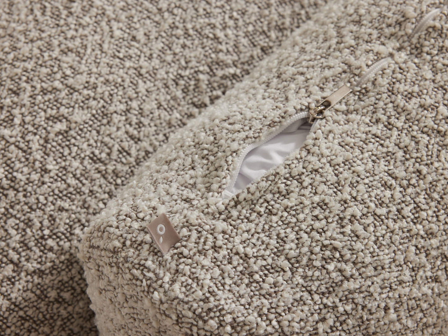 Close-up of beige textured fabric with an open zip revealing white lining. Ideal for furniture upholstery like sofas or cushions.