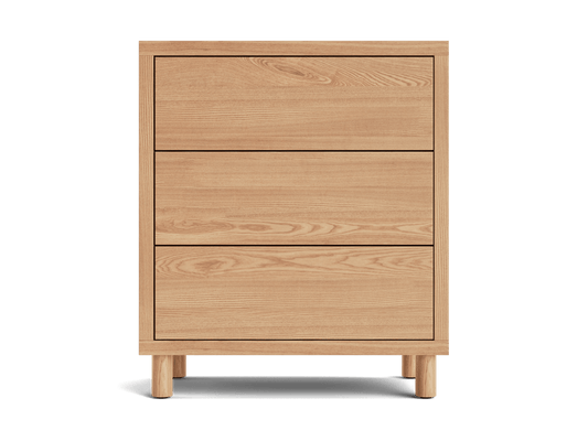 Wooden chest of drawers with three panelled drawers. Light brown wood with visible grain. Rectangular shape on short legs.