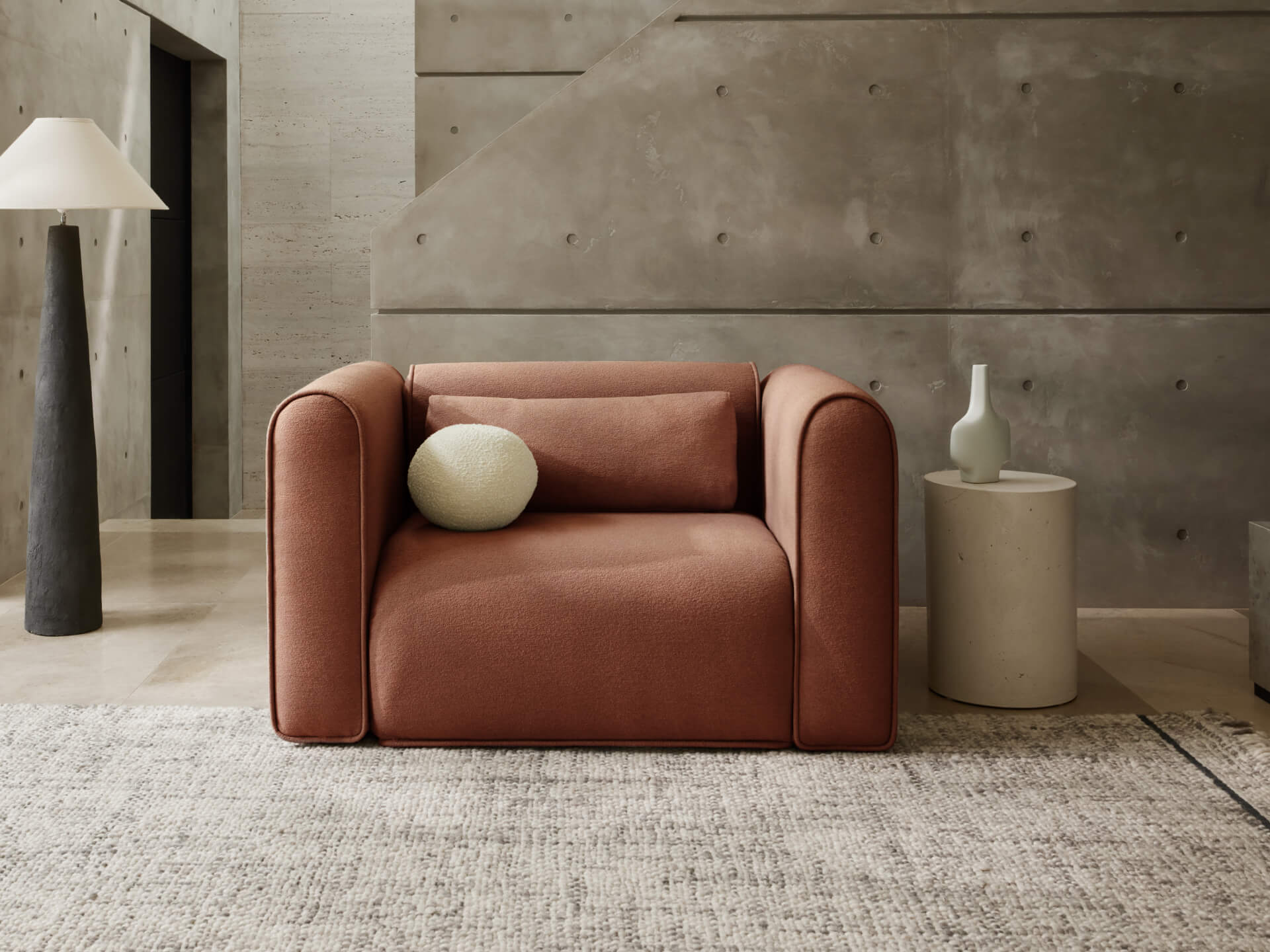 Modern lounge featuring a brown armchair with a white cushion, a round beige side table, and a tall grey lamp on a light rug.