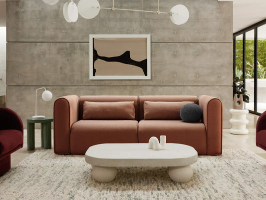 Modern living room with a brown sofa, light grey oval coffee table, abstract wall art, and circular chandelier, featuring minimalist decor.