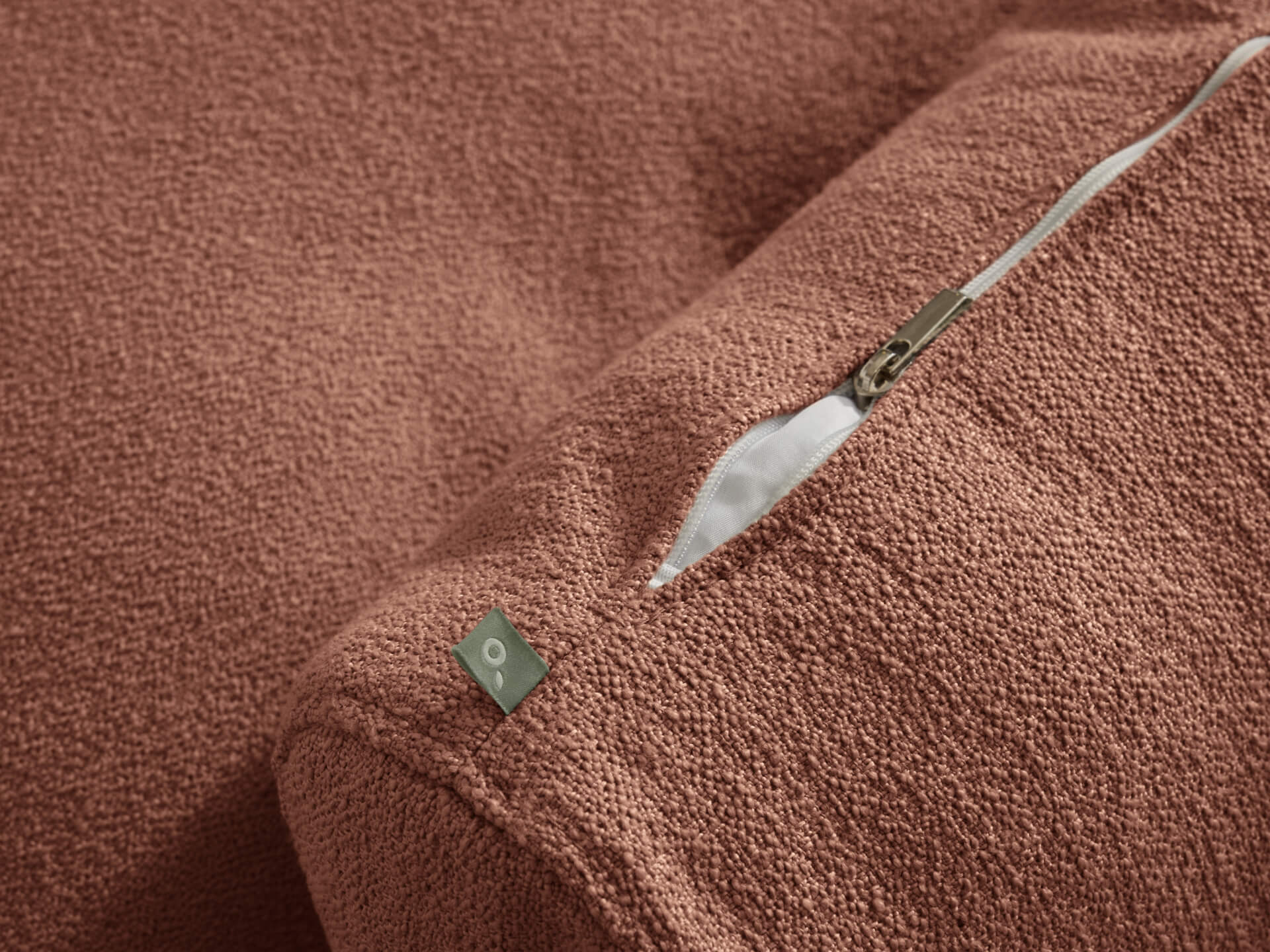 Close-up of a textured brown fabric cushion with a visible zipper and a small metallic tag.