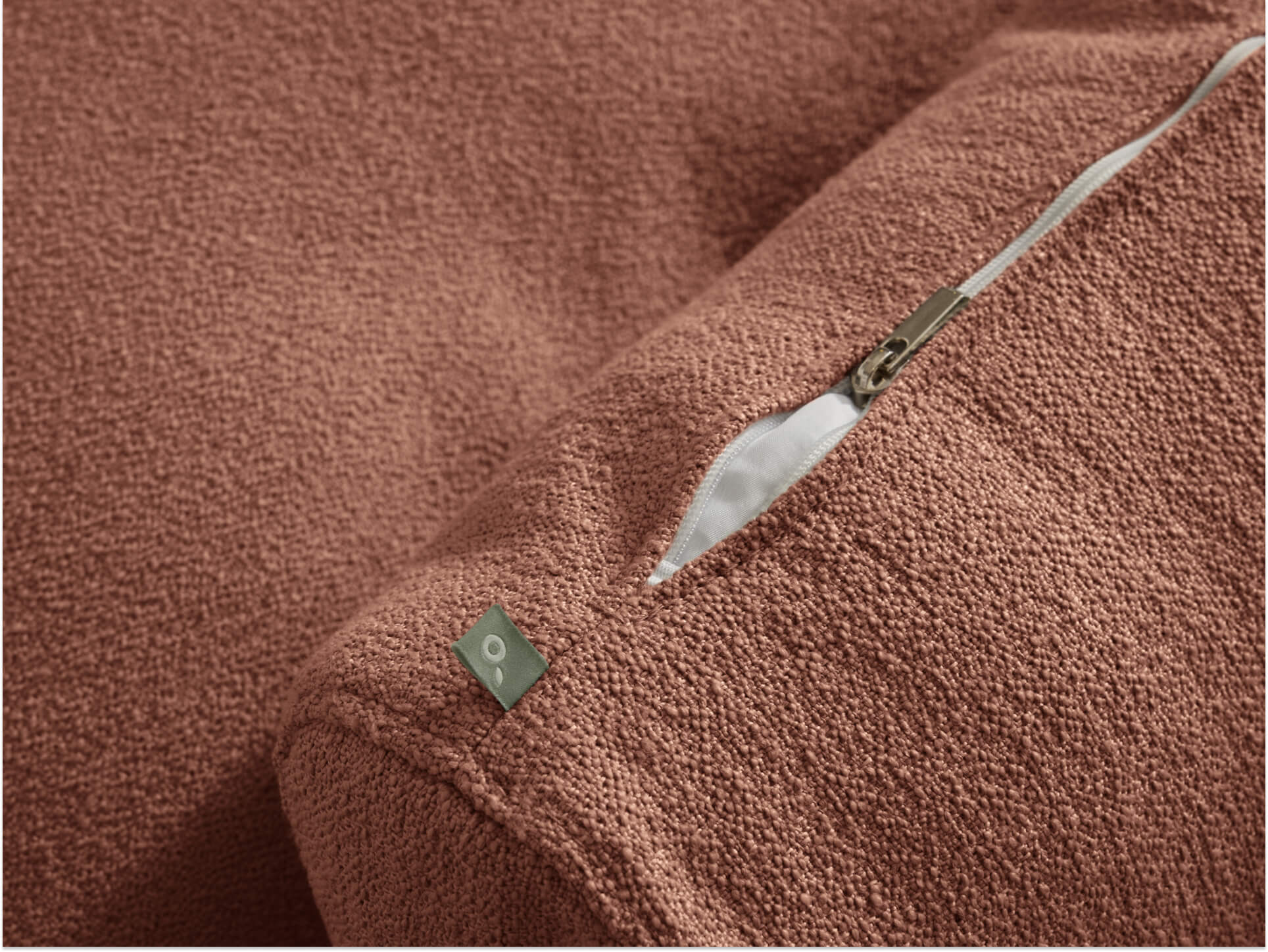 Close-up of a brown textured fabric cushion with a visible zipper and small metal tag.