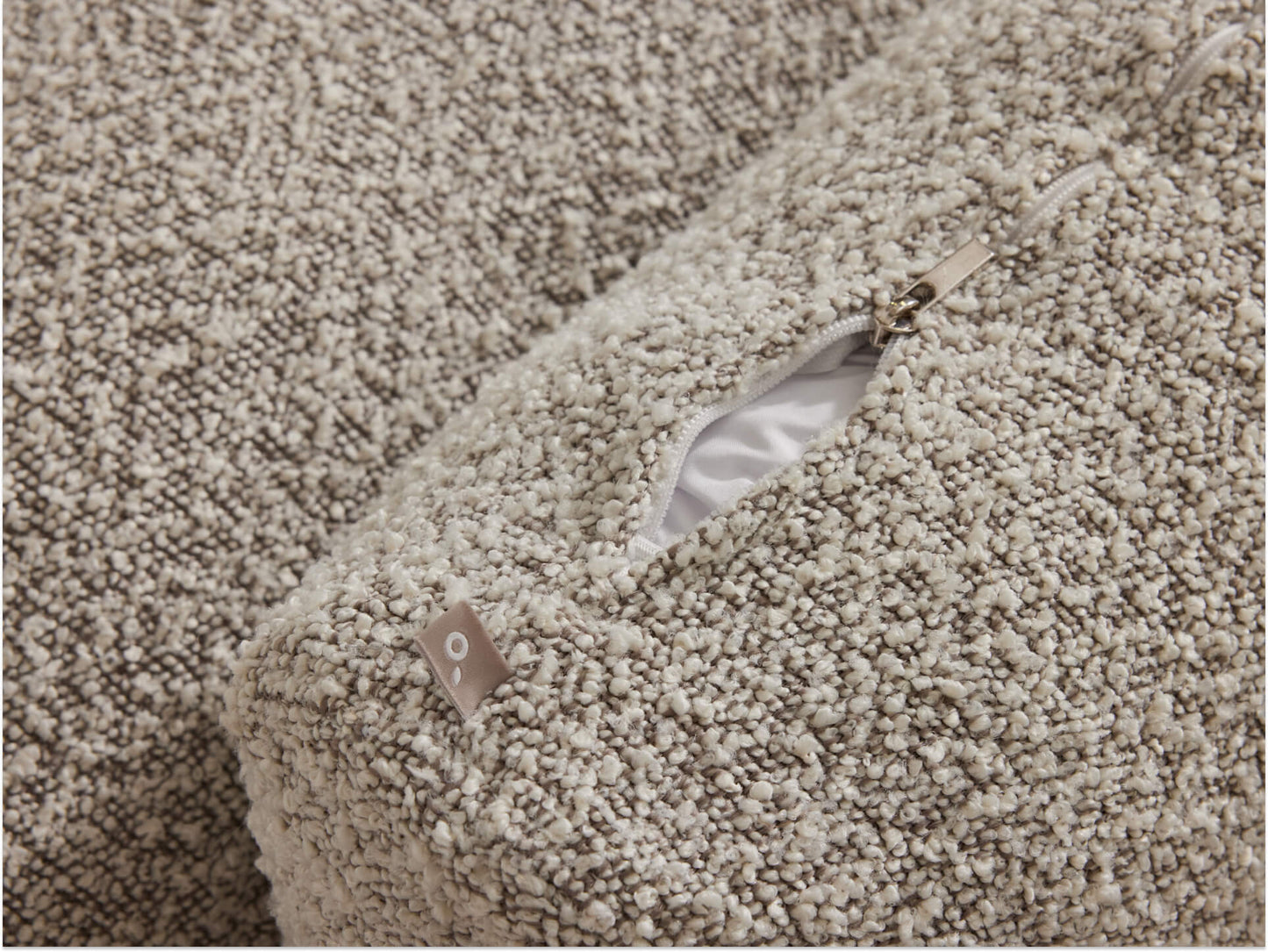 Close-up of a beige textured fabric cushion with a visible zipper and white lining.