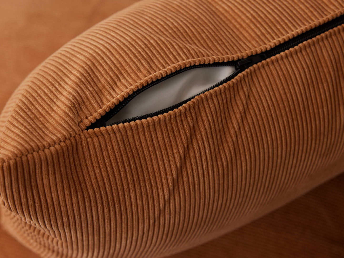 Close-up of a brown corduroy cushion with a visible black zipper opening, revealing a white inner lining.