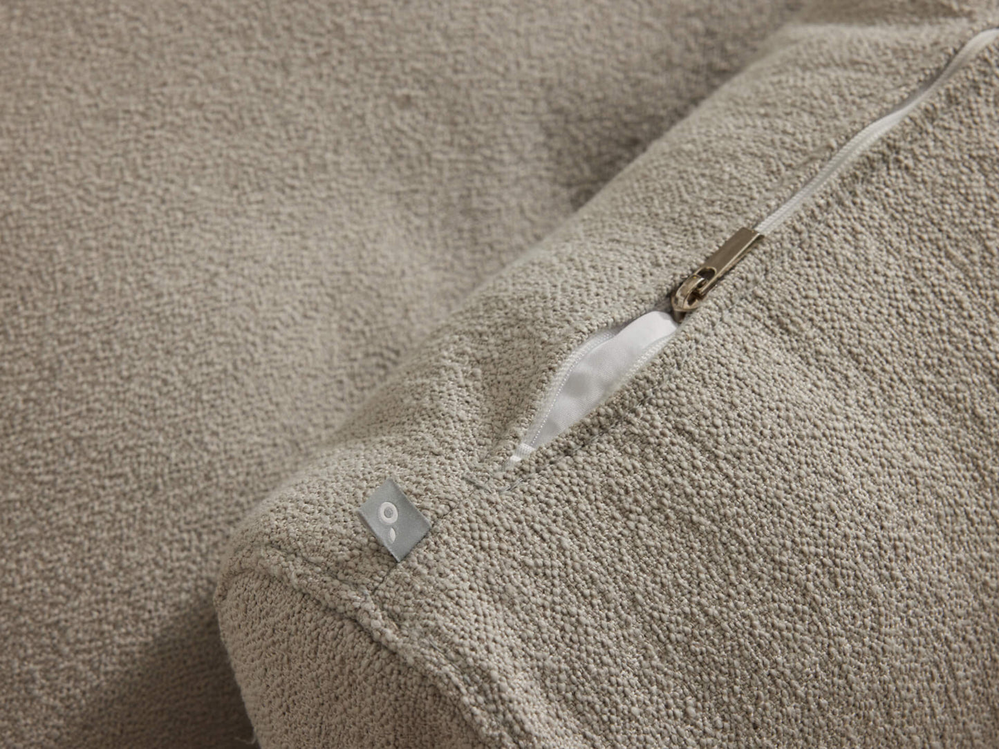 Close-up of textured beige cushion cover with a visible gold zipper, partially open, revealing a white lining.