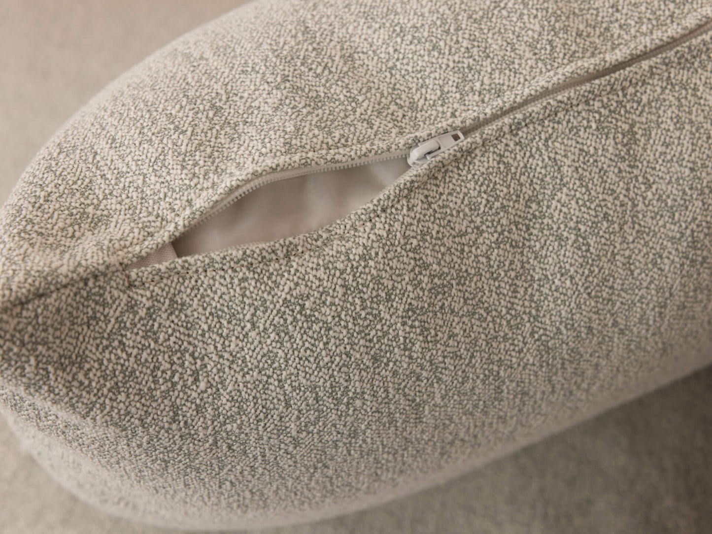 Close-up of a textured light grey cushion cover, slightly opened to reveal a zip.