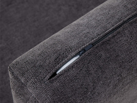 Close-up of a dark grey fabric sofa cushion with an exposed black zipper, showcasing texture and design detail.