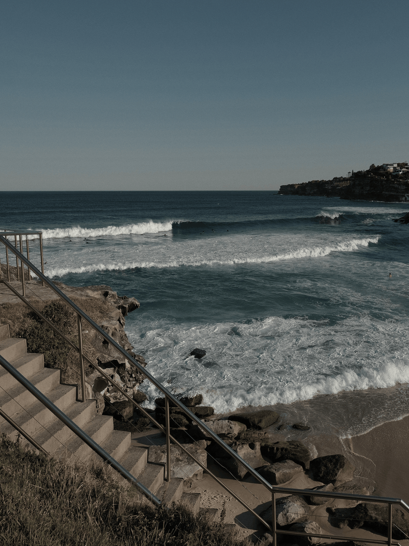 Australian coastal beach with concrete steps leading to surf and headland in background