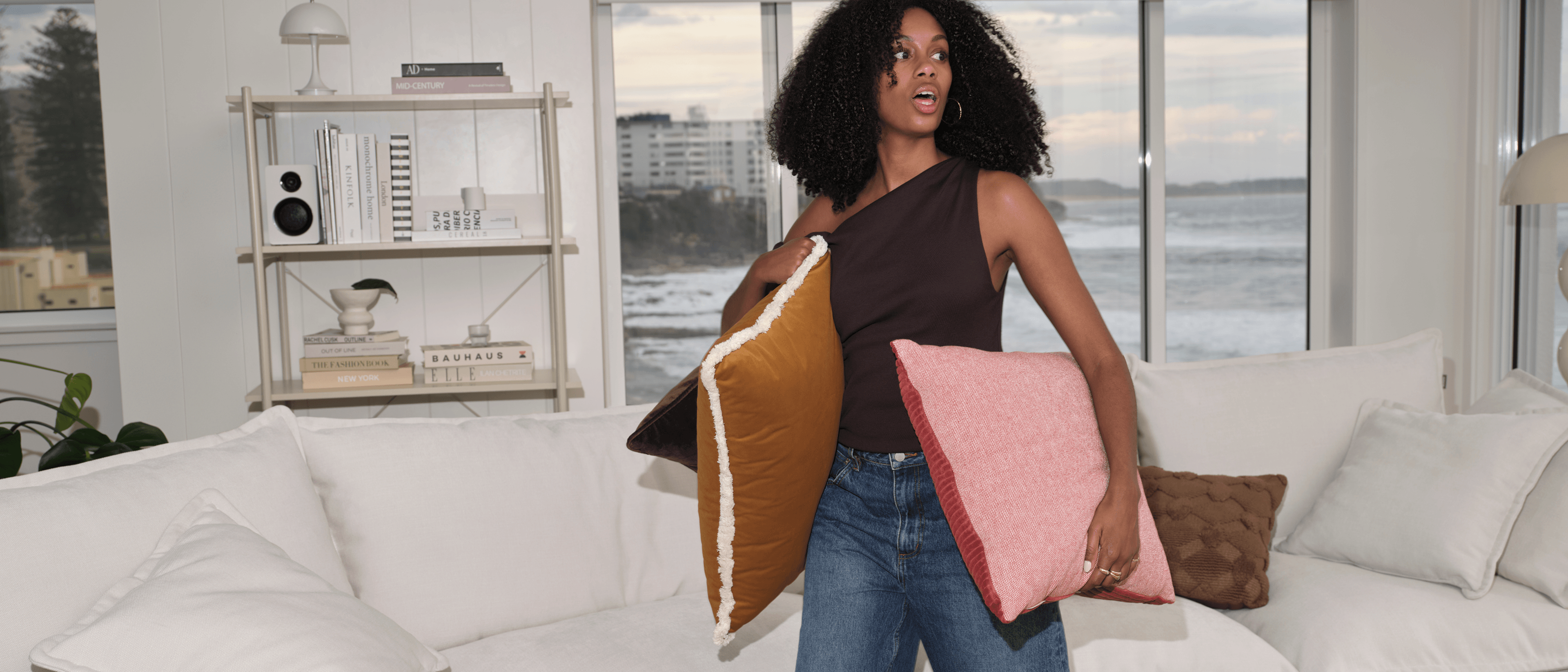 Woman carrying colourful accent cushions beside white Koala Tamworth sofa in coastal living room