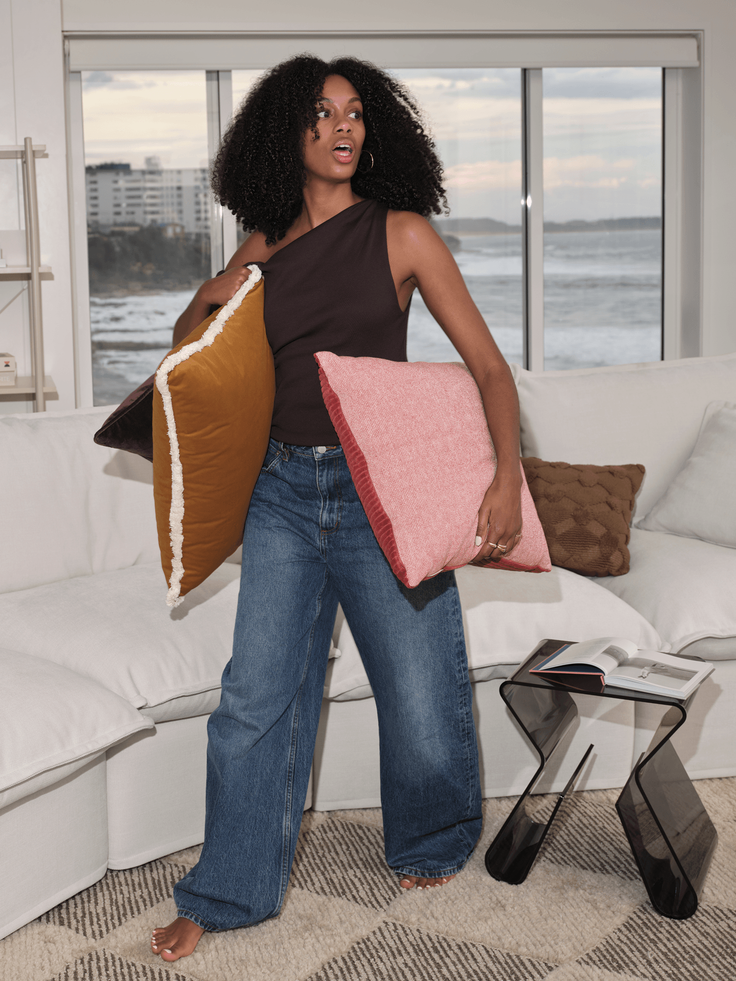 Woman standing with colourful accent cushions beside white Koala Tamworth sofa with ocean backdrop