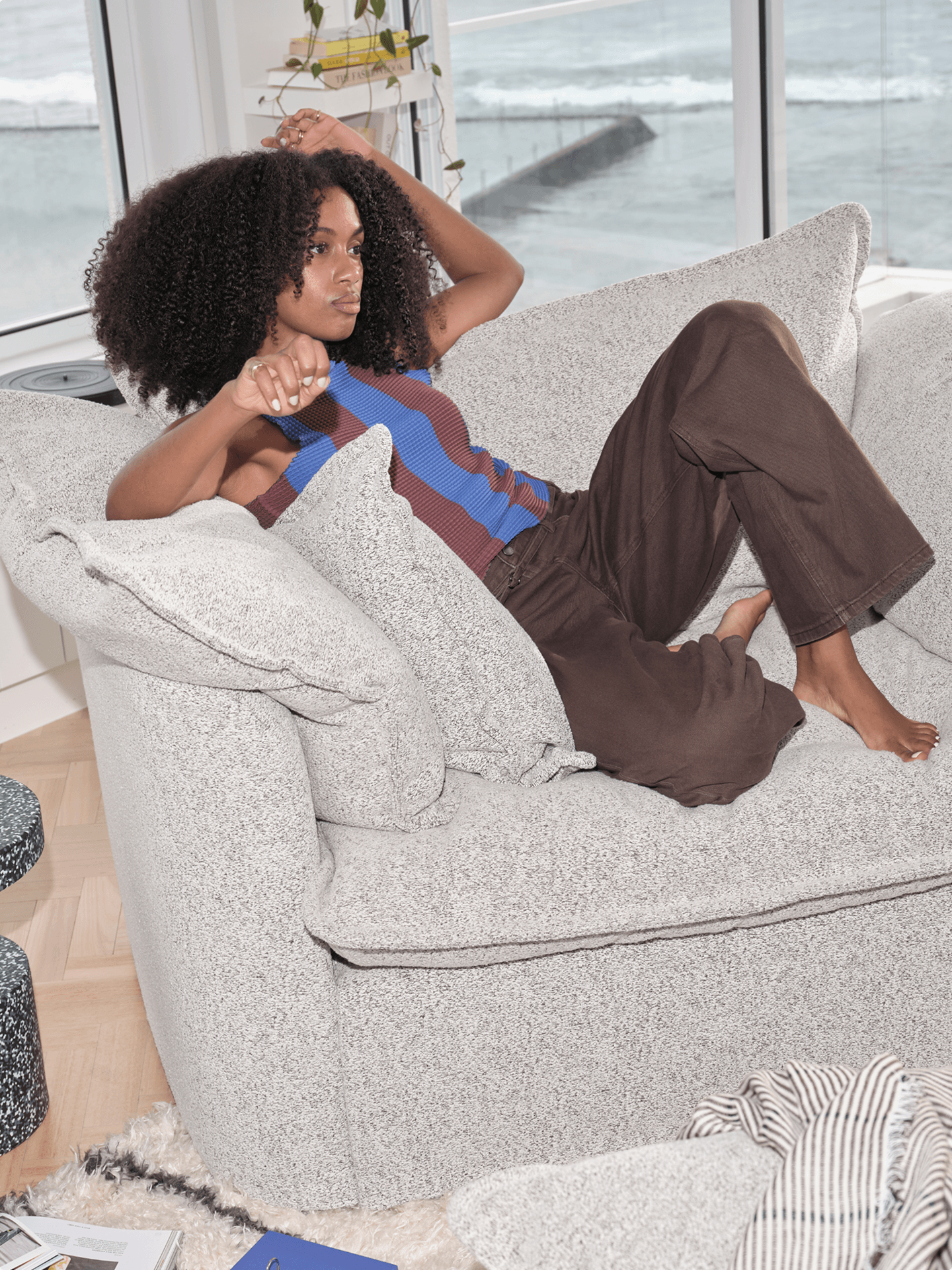 Woman lounging on cream boucle Koala sofa with ocean views through windows