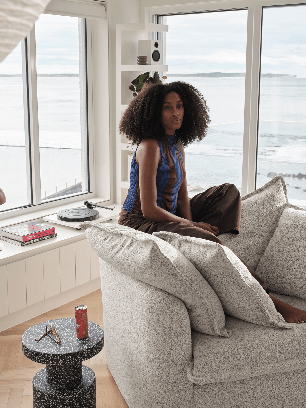 Woman sitting on cream boucle Koala sofa in coastal living room with ocean views and vinyl player